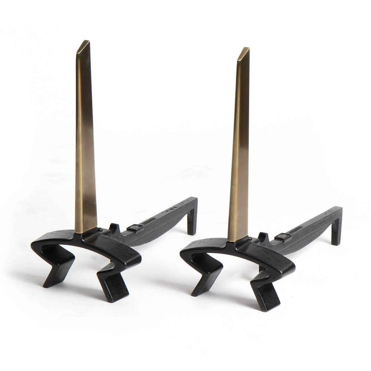 A pair of sculptural patinated bronze andirons having simple diagonally cropped tapered blades projecting vertically from footed cast iron bases.