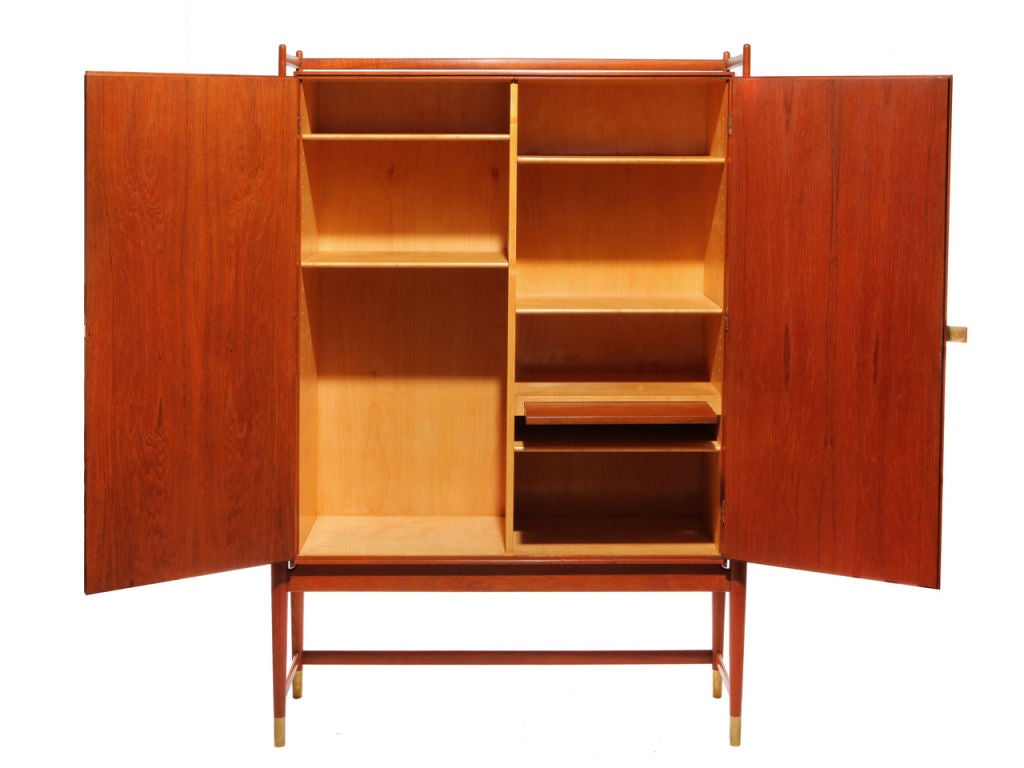 An unusual custom two-door cabinet in teak, having an architectural exposed framework supporting the floating case element. With brass hardware and feet, and five concealed and adjustable shelves, along with a single stationary shelf with pullout