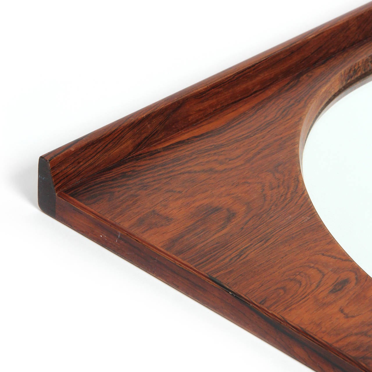 A finely crafted and proportioned wall mirror having a circular mirror centered in an expressive Brazilian rosewood frame with raised and beveled side rails.
