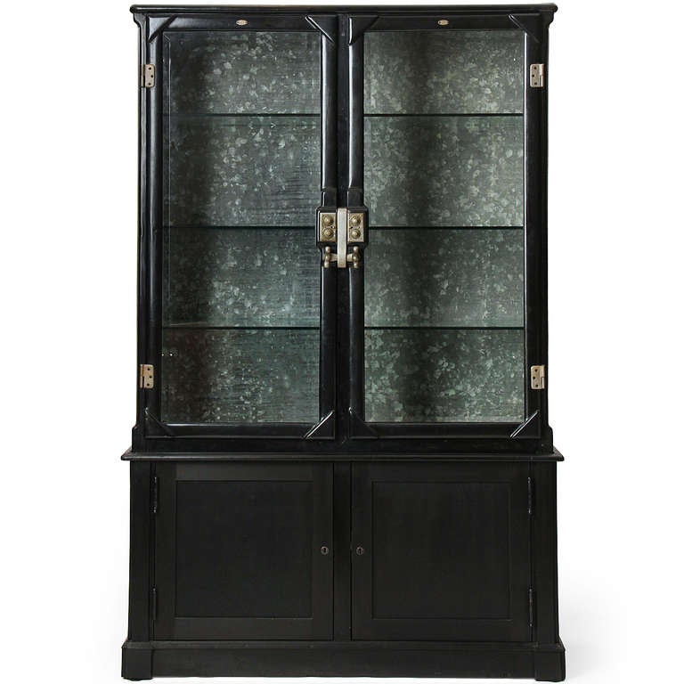 A stately and superbly crafted cast iron and glass display cabinet having working combination door locks, beveled glass front and side windows and galvanized steel back wall, resting upon an ebonized wood base with storage. USA 1890-1900