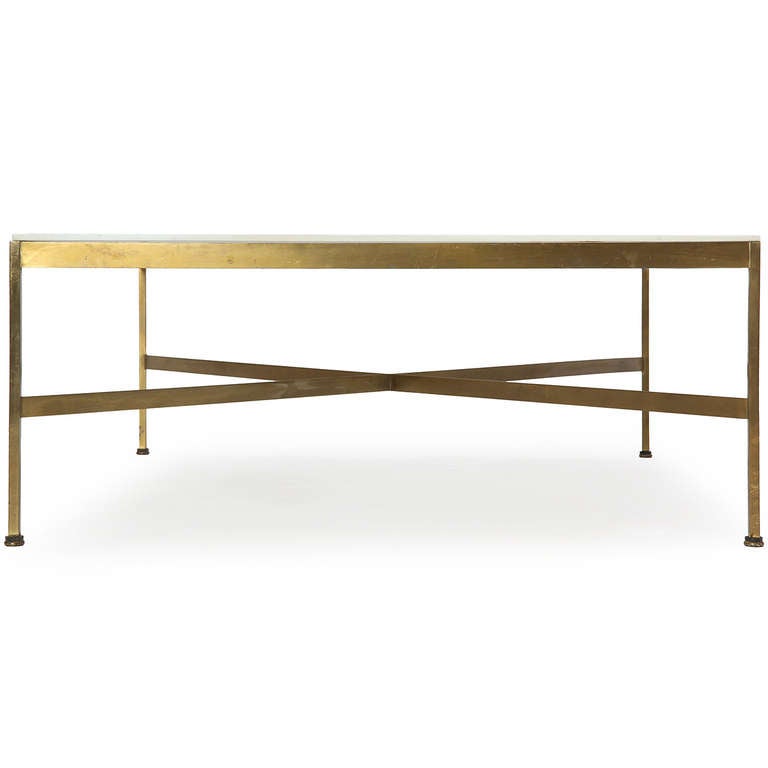 A minimalist low table with a brass frame, an X stretcher support and a white glass top.