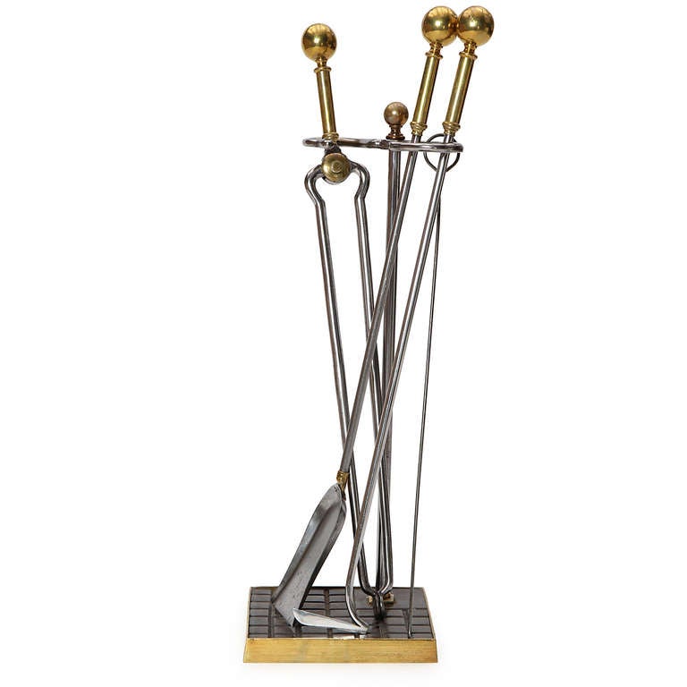 An elegant set of firetools with brass handles and upright stem to hold tools which rest on a gridded cast iron base.