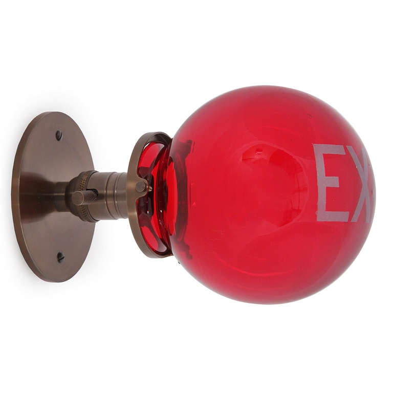 A simple wall-mounted sconce with brass hardware and a blown red glass globe with painted EXIT.