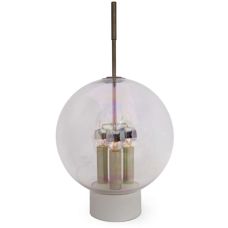 A sculptural table lamp with three candle like sockets surrounding a center stem that protrudes from a glass sphere globe.