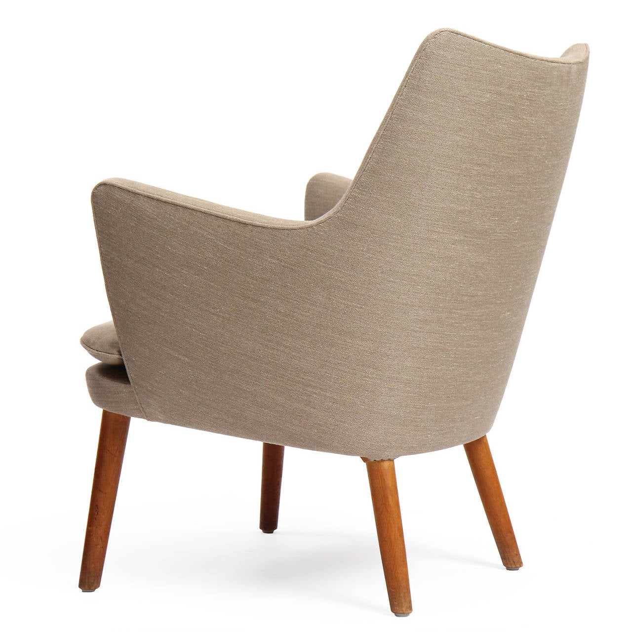 An elegant and sculptural lounge arm chair having a tight upholstered back and loose seat cushion that sits on solid oak tapered dowel legs.