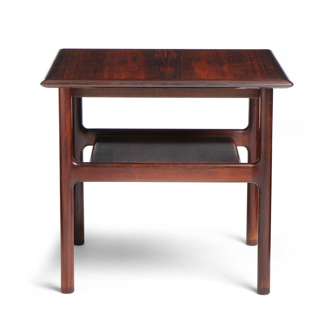 A fine substantial and architectural end table in richly grained Brazilian rosewood having a square top and floating shelf.