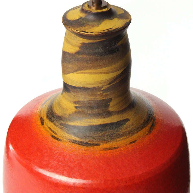 A hand thrown ceramic wide bottle-form lamp in a striking and unusual glaze pattern: Umber and earth-toned swirls sandwich a wide swath of apple red.