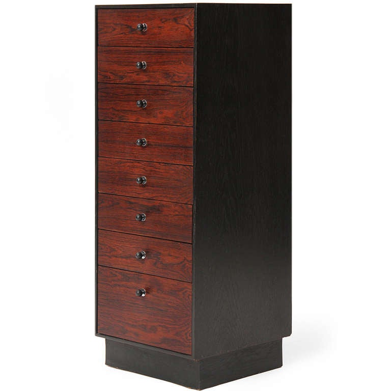 An uncommon tall and narrow cabinet in rosewood and tinted ash, having shaped bullet pulls with chromed escutcheons and eight vertical drawers rising over a plinth base.