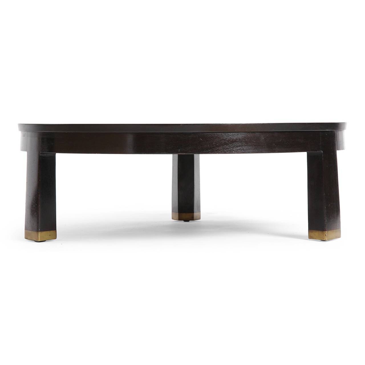 A fine and substantial ebonized mahogany low table having a circular top with a recessed apron floating on three reverse tapered legs with brass feet.