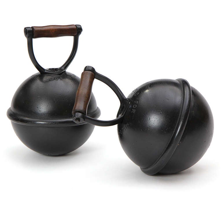 An excellent pair of early mass produced kettlebells in patinated iron with a wood handle and originally designed with the ability to adjust the mass via interchangeable internal weights.