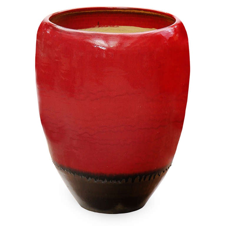 A vibrant and massive red glazed planter with a single hole in the bottom for drainage.