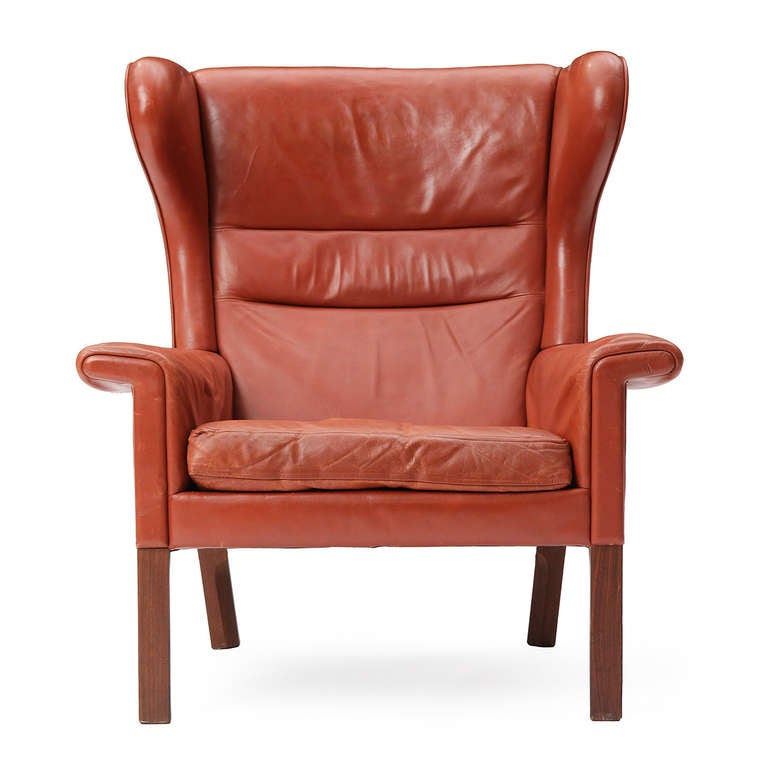A rolled arm wing easy chair with a generous leather seat and cushioned back with squared legs.