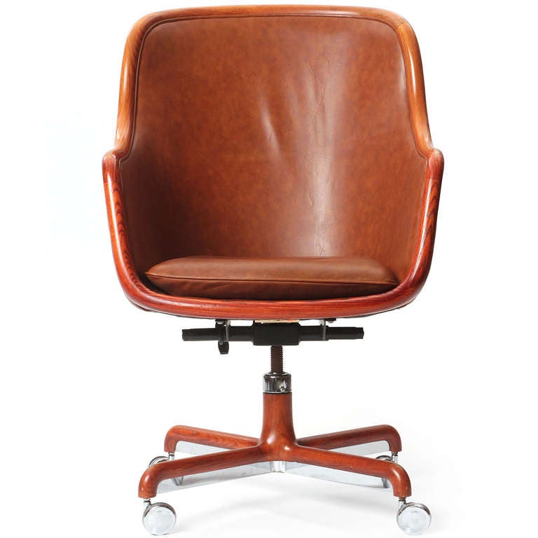 A barrel-back desk chair with the original brown leather upholstery and bent wood edging, on an X-base with casters.