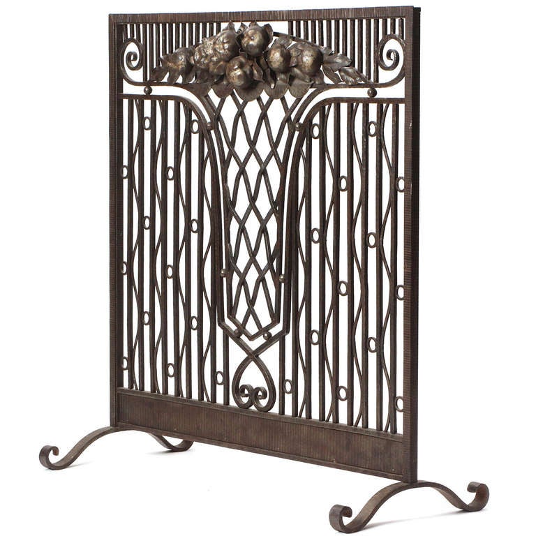 An Art Deco wrought iron fire screen having hammered and gilded surface work and a central motif depicting a vase holding a bouquet of flowers. Attributed to French master metalworker Paul Kiss.