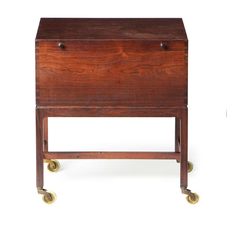 An excellent rosewood cabinet with box cut joinery, interior divided trays, and open storage atop slender legs on brass castors.
Designed to be a desk accessory, sewing box, or bar cart.