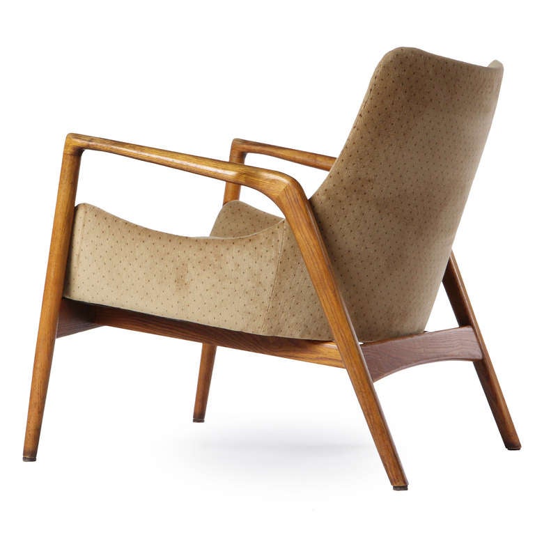 An architectural lounge chair with an exposed elegant solid oak frame and a shaped and floating upholstered seat.