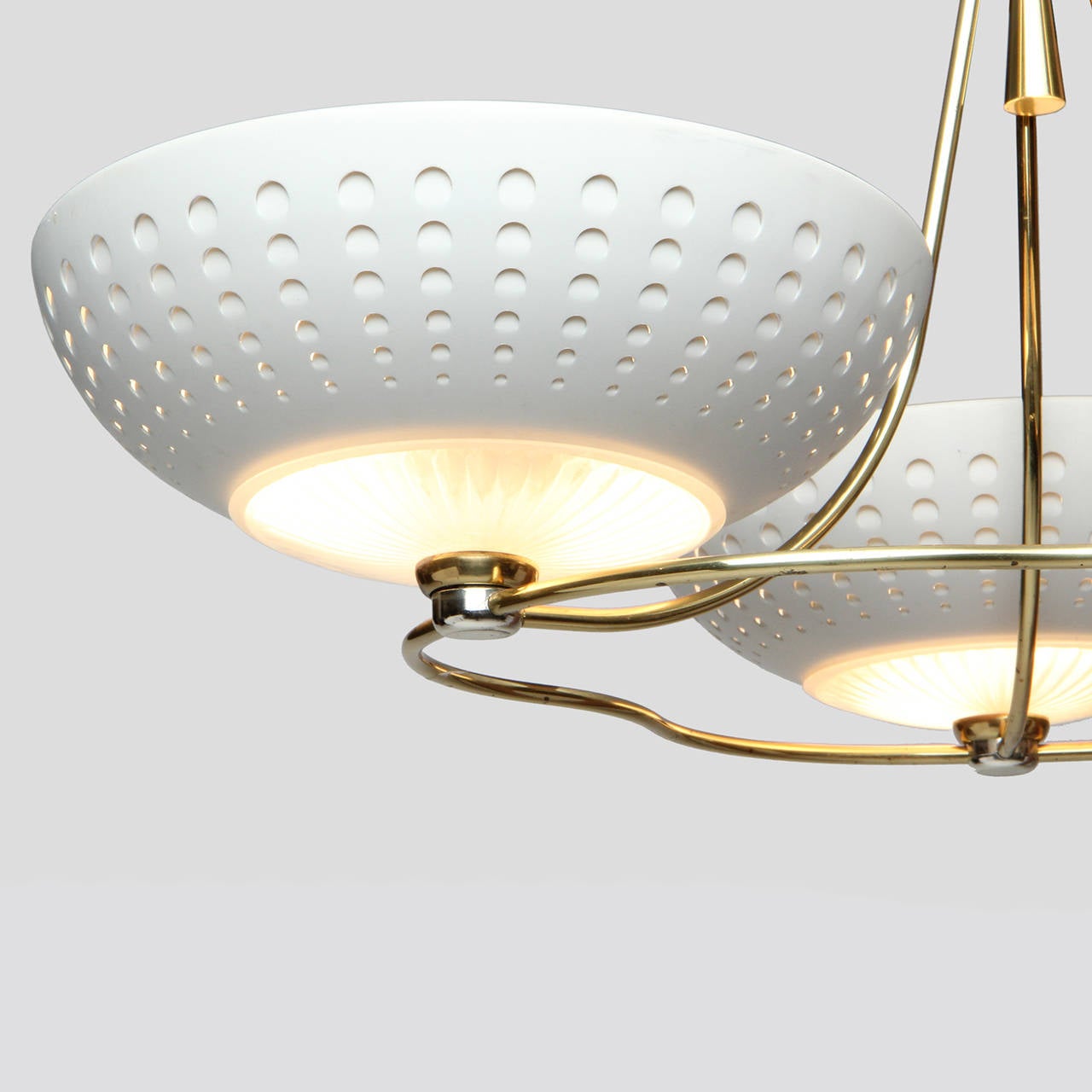 An interesting, beautifully proportioned and finely detailed chandelier having an expressive and sculptural lacquered brass armature supporting three cream lacquered and perforated uplights.