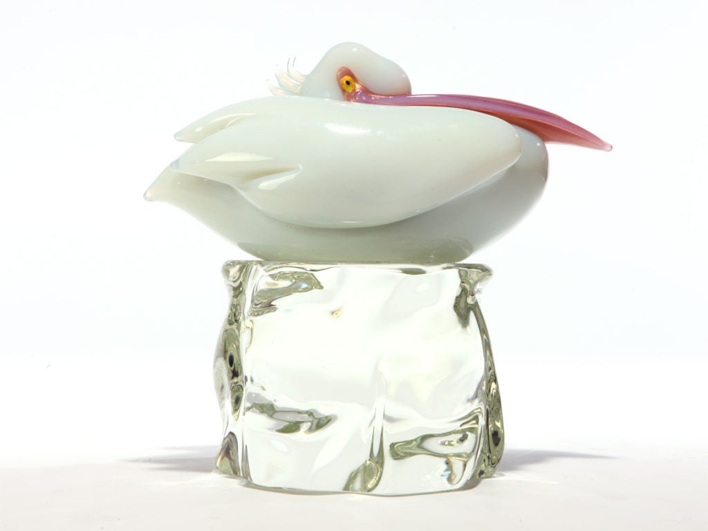 An opalescent white glass pelican resting on a clear crystal perch.