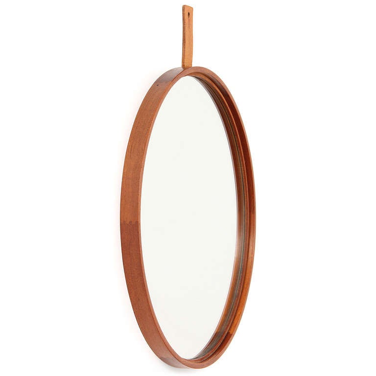 Useful jewelry for the wall: A crisp circular wall mirror having a precise thin teak frame which is suspended by a pierced leather tab.