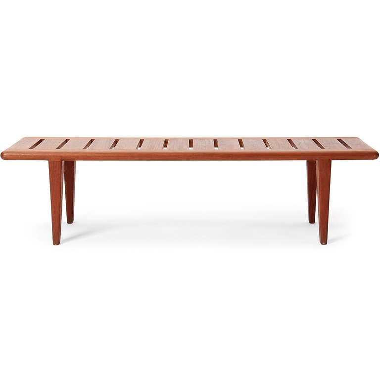 A solid teak bench with a slatted seat and tapered legs.