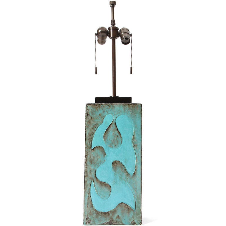 A unique table lamp having an evocative and finely executed abstract relief rising from a substantial rectangular clay body with a rich variegated iridescent turquoise glaze.
