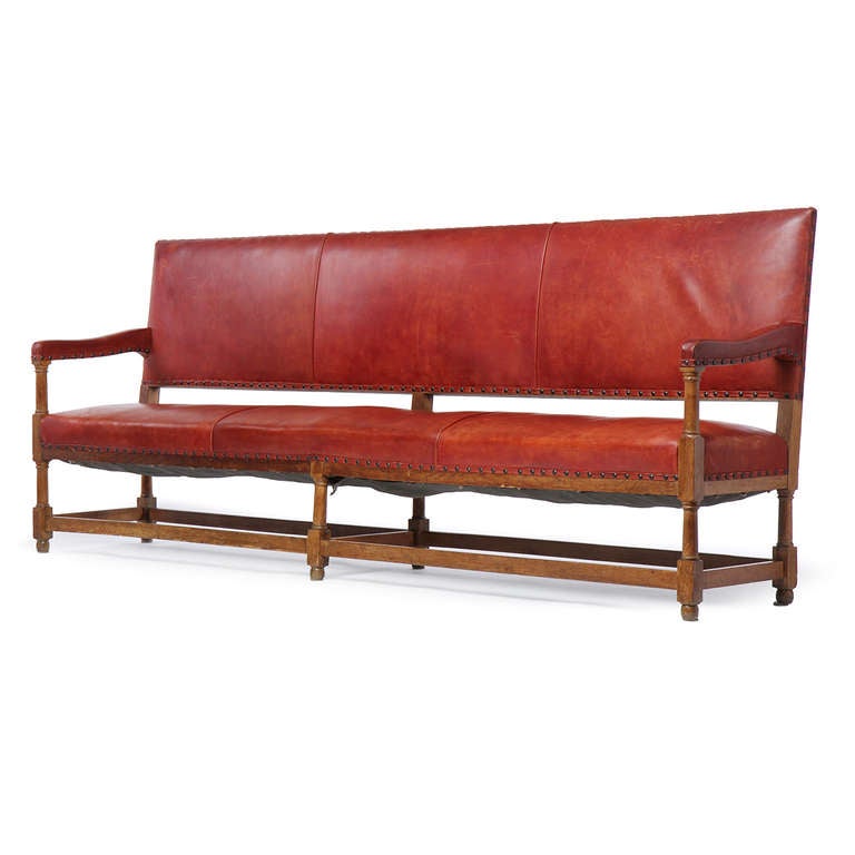 An outstanding and beautiful bench with an exposed hand-carved oak frame wrapped in Ox hide leather with a rich red patina and large brass nail head trimming.