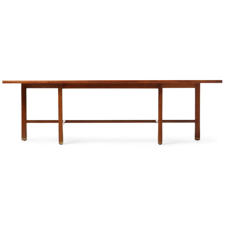 A low console or table with a spare mahogany frame that supports an asymmetrical top with brass capped feet.