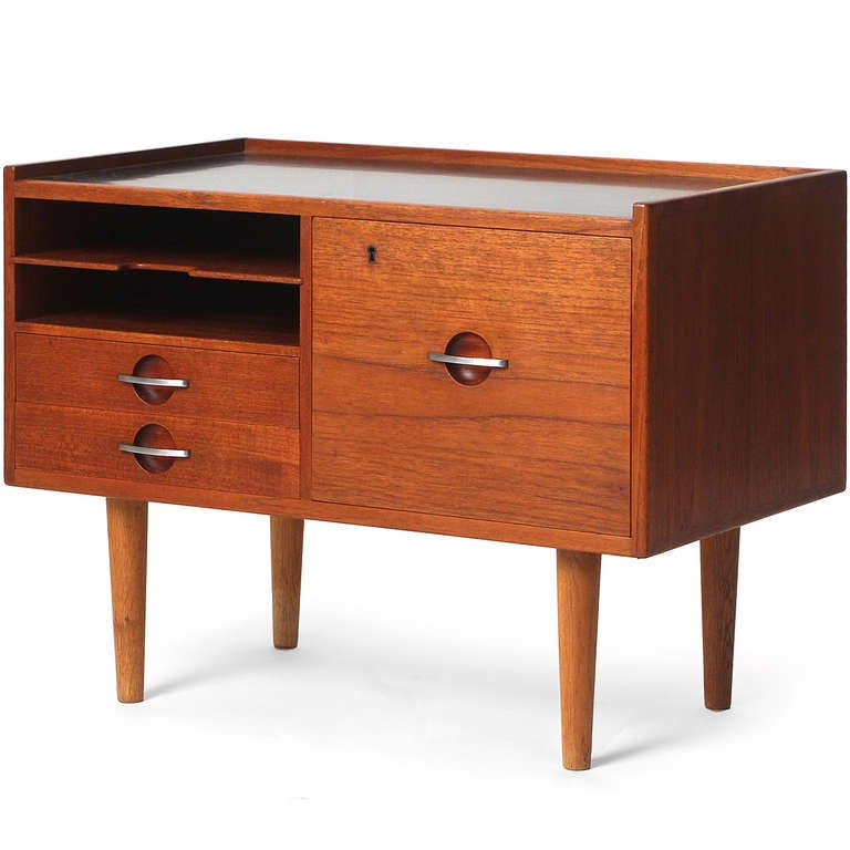 A finely fabricated 'Telephone Table' cabinet in teak having a black laminate top with turned oak dowel legs and Minimalist steel recessed pulls. There is a keyed hanging file drawer on the right with two smaller drawers and open paper slots on the
