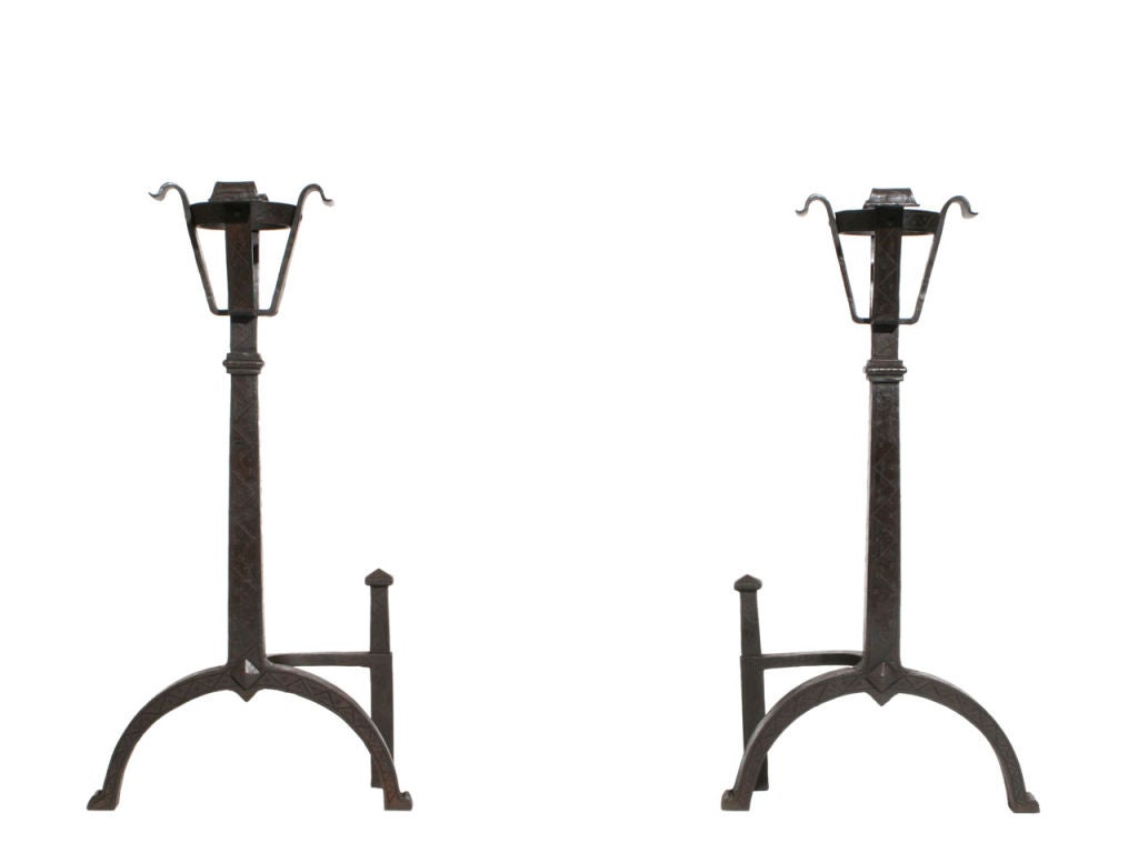 An over-sized set of wrought iron andirons topped with  baskets large enough to hold and warm bottles of brandy. Etched pattern is repeated on matching set of fire tools.