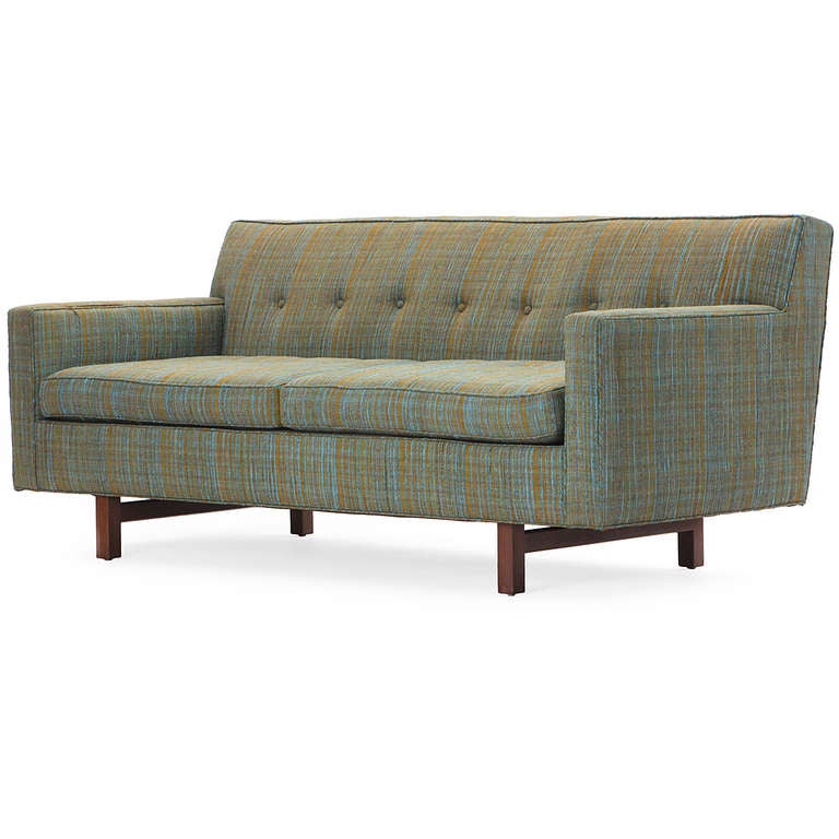 A tight-backed and fully upholstered even-armed sofa having a dowel legged mahogany base and retaining its original textured button-tufted upholstery.
