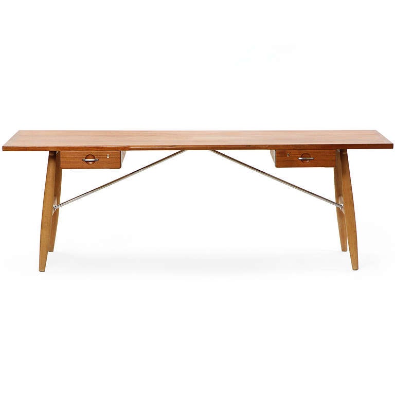 A refined, rare, beautifully proportioned and masterfully executed writing desk having a solid teak top over twin floating drawers, resting on turned dowel legs in oak, the entire structure braced by architectural satin-finished angled steel rods.