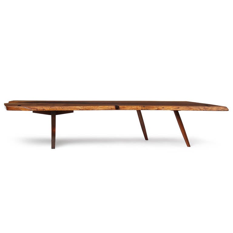 A dramatic and impeccable studio-made low table having a solid and highly figured free-edged black walnut top joined with three rosewood butterfly tenons, floating atop a carved slab base with two staggered splayed dowel legs.