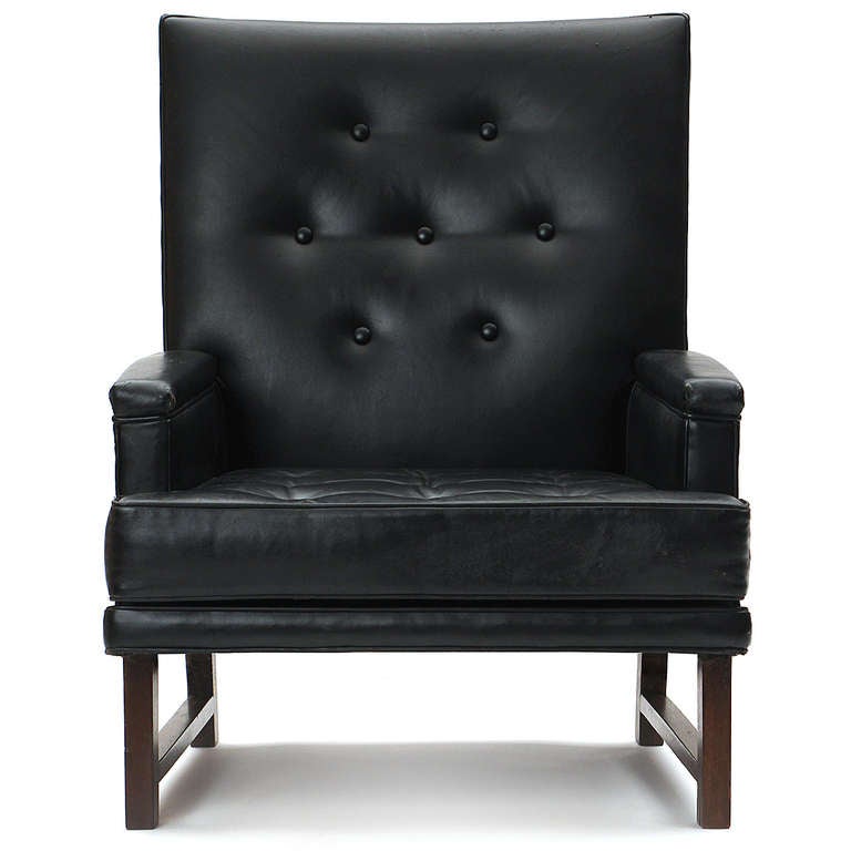A high backed, button-tufted lounge chair in the original black leather upholstery with mahogany legs and side stretchers.