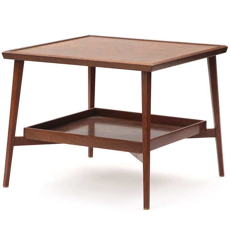 A tailored two-level square end or lamp table in walnut having splayed tapering legs.