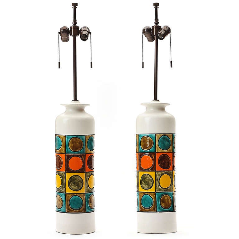 A joyful and expressive pair of ceramic table lamps of columnar form having a hand-painted multi-color circle-in-a-square motif decoration.

Base is 20.5