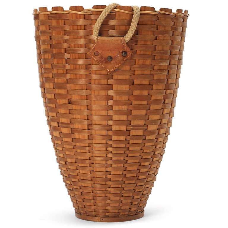 A hand-built tapering basket of slatted split hickory that retains its original braided rope handle attached to the basket by leather tabs.