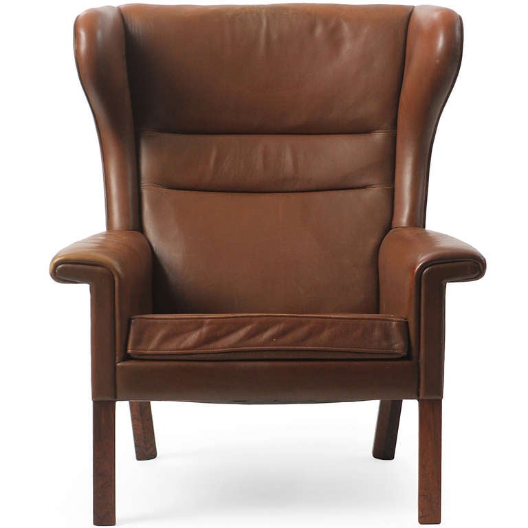 A well-proportioned, elegant and highly comfortable rolled arm wing chair having squared solid rosewood legs and masterfully covered in supple natural tan leather. Designed by Hans J. Wegner, cabinetmaker A.P.Stolen. A matching ottoman is available.