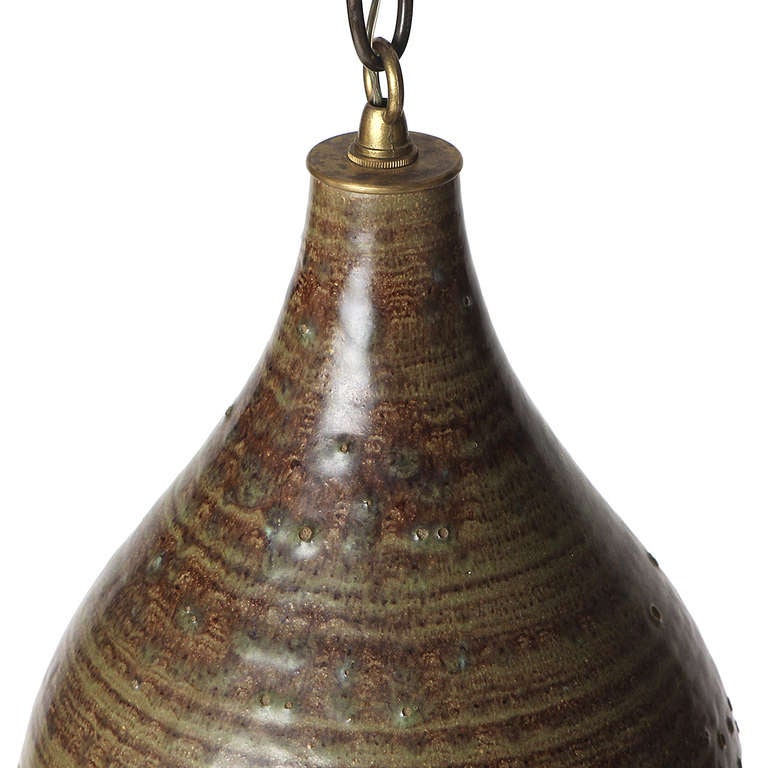 A hand thrown ceramic pendant lamp with a brown and green glaze and four staggered rows of pierced openings. Measurements are for fixture only. Drop is adjustable.