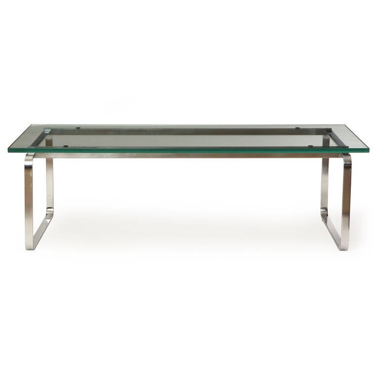 A rare low table with two simple continuous brushed stainless steel band legs supporting a clear glass top.
