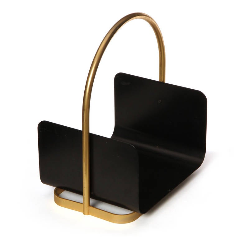 A simple and architectural log holder with an arched tubular brass handle and a bent black steel tray.