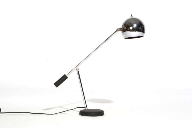 A fully adjustable chrome articulating desk lamp having a pivoting spherical shade on round black disc base.