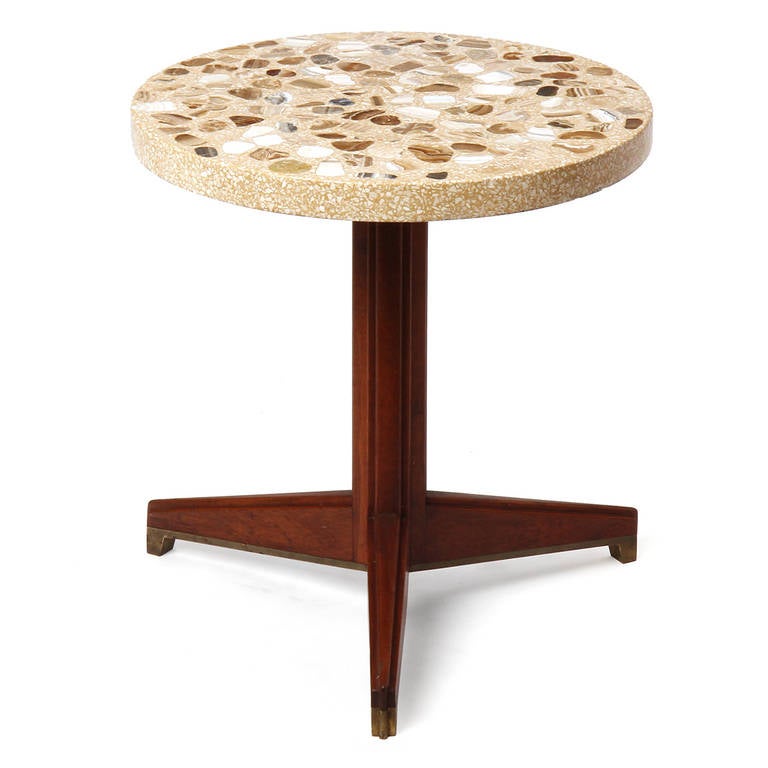 An occasional pedestal table having a geometric walnut and brass tripod base supporting an expressive mosaic stone top with selections of geodes.