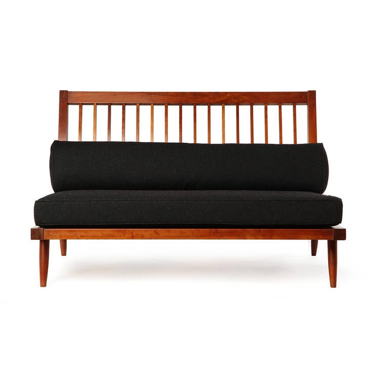 A fine and uncommon George Nakashima studio made slat back settee in rich walnut and having charcoal upholstery.