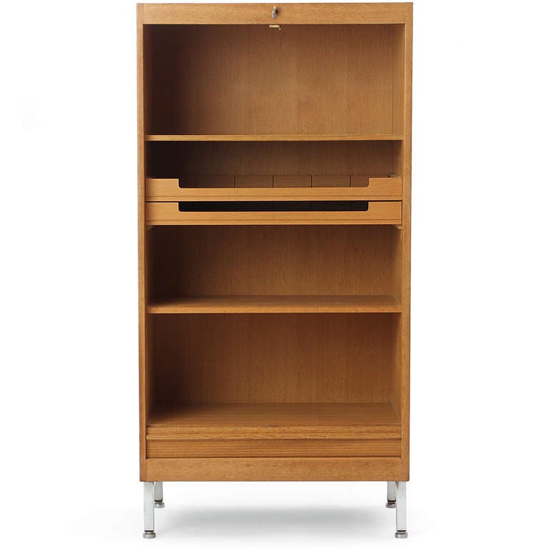 An oak cabinet with tambour door concealing open storage with shelves, on metal legs.