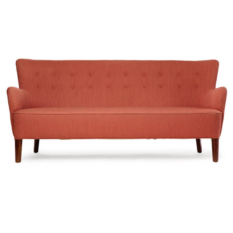 A tailored and sculptural high-backed button-tufted sofa, the upholstered body resting on substantial turned teak dowel legs.