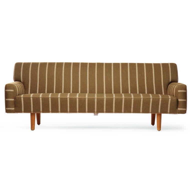 A sculptural, tailored and fully upholstered sofa floating on well-scaled turned oak dowel legs and retaining its original striped wool fabric.