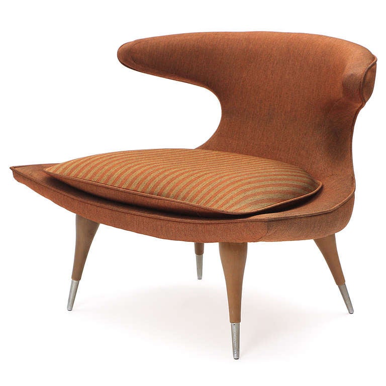 A sculptural and unique lounge chair of good scale having a cinched waist and wrap-around back, tapered and brass-capped walnut legs, and upholstered in a butterscotch wool with a loose seat cushion in a complementary striped pattern.