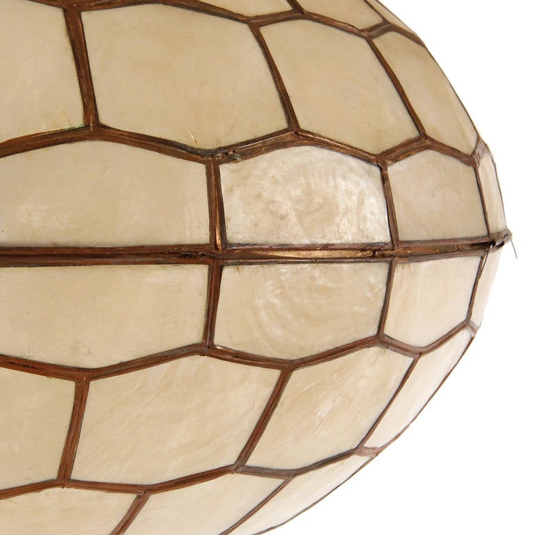 An unusual and beautiful hand-crafted circular ceiling pendant made of warmly iridescent capiz shells set into a geometric bronze framework.