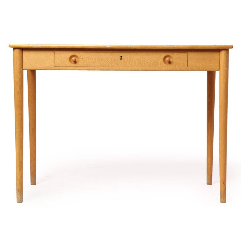 An elegantly simple writing desk in expressive white oak having a single locking drawer with recessed knob pulls.