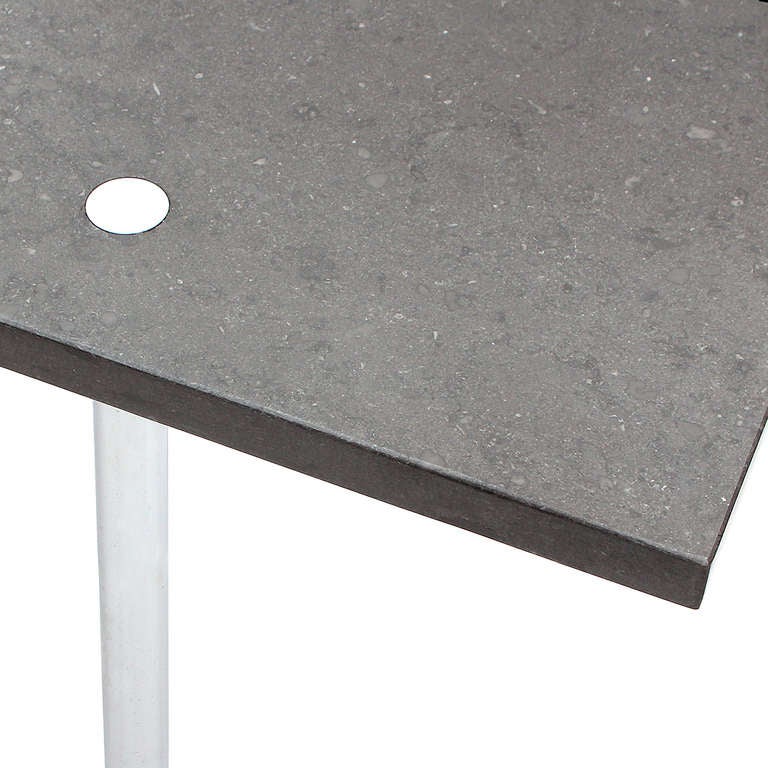 A Minimalist desk or table fashioned from a rectangular slab of black granite perforated by stainless steel column legs.